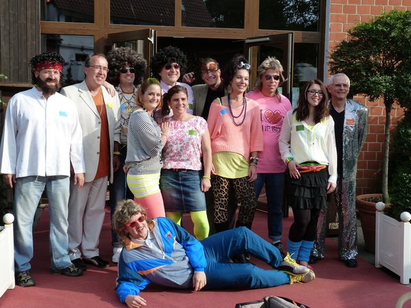 Die Gäste unseres Quizzes TeamDuell haben sich zum Gruppenfoto versammelt und tragen 80er Jahre-Kleidung.